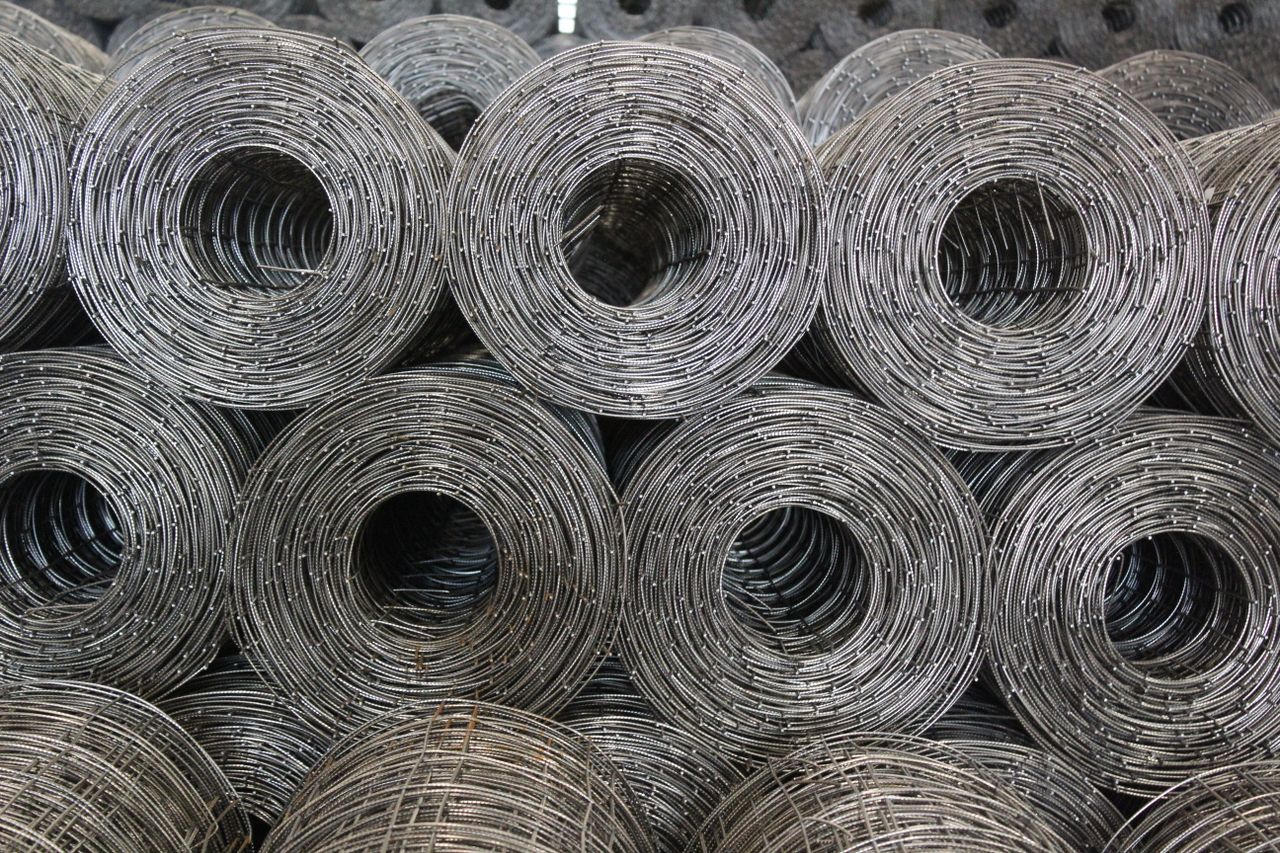 Stacked coiled steel wire mesh rolls captured in a warehouse setting.